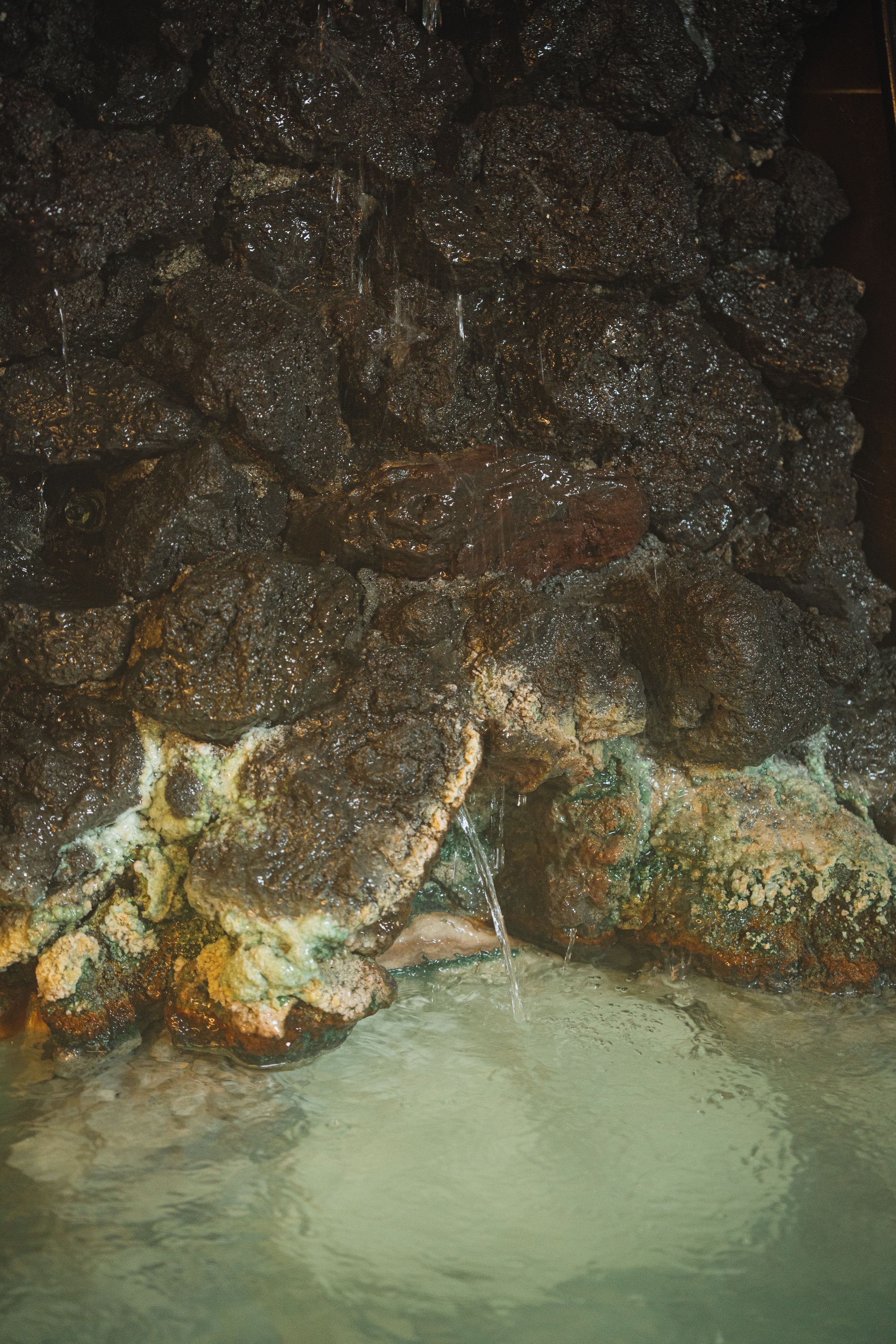 A cave interior with water flowing over rocks and into a pool.
