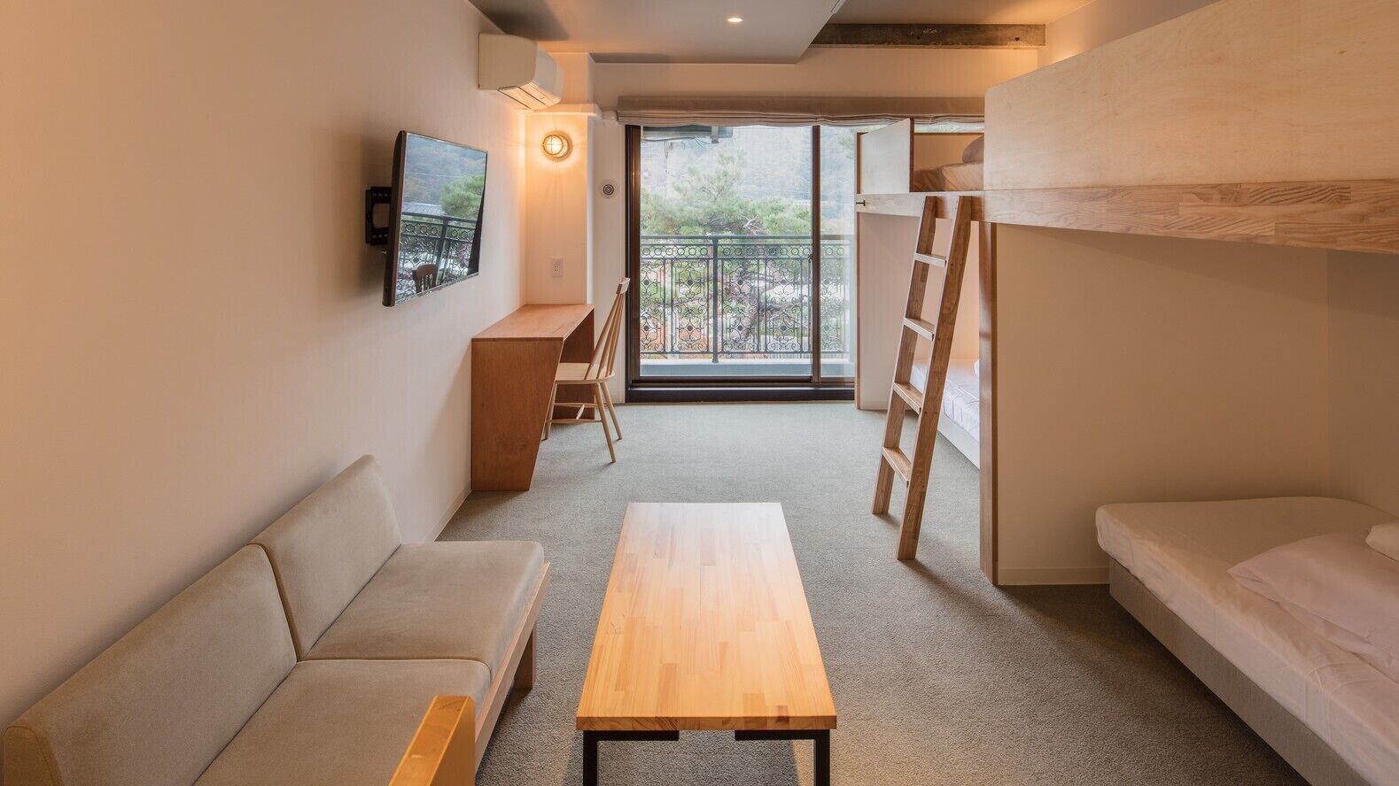 A room with a sofa, a wooden table, a bunk bed, a ladder, a desk, and a balcony with a railing.
