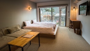 Un dormitorio moderno con cama, sofá, escritorio y balcón con vistas a árboles.