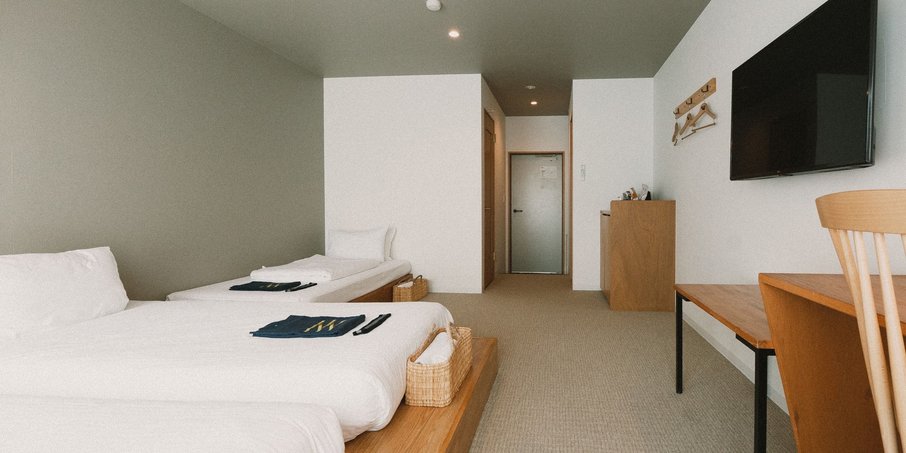 A hotel room with two single beds, a desk, a chair, a television, and a door leading to a bathroom.