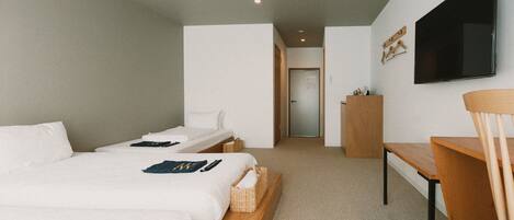 A hotel room with two single beds, a desk, a chair, a television, and a door leading to a bathroom.