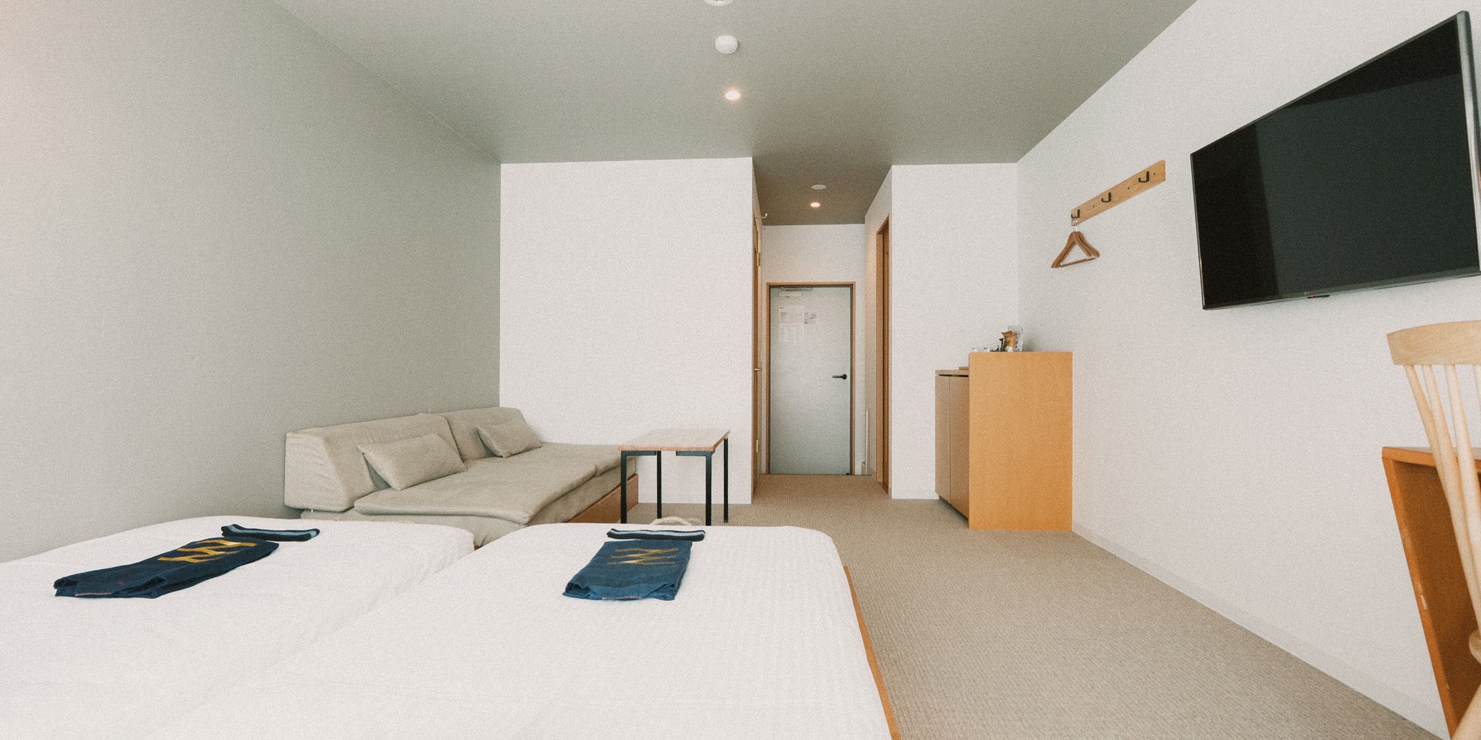 A hotel room with two beds, a sofa, a TV, and a desk.