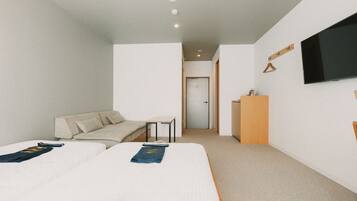 Ein Hotelzimmer mit zwei Betten, einem Sofa, einem Fernseher und einem Schreibtisch.