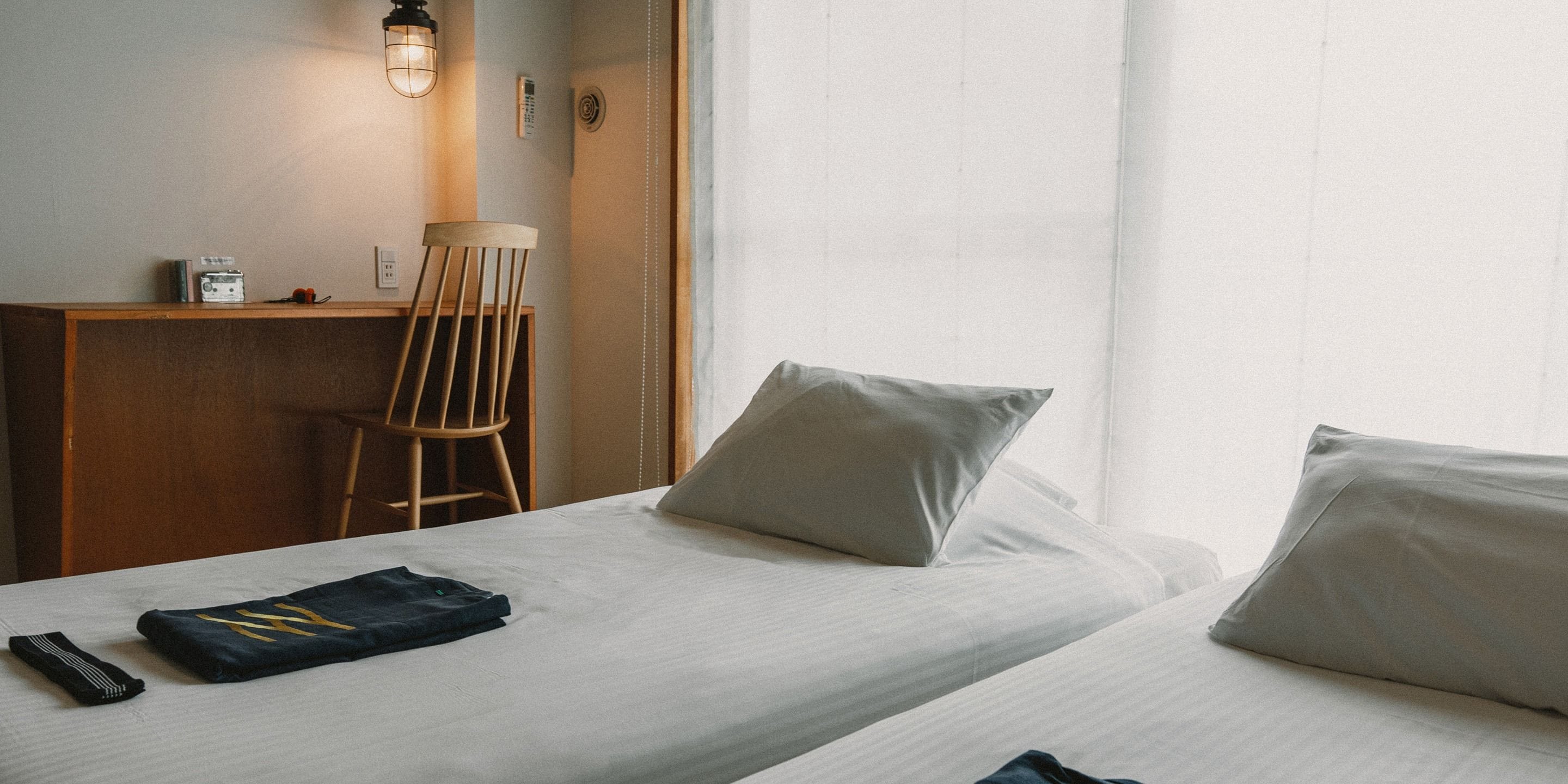 Une chambre d’hôtel avec deux lits, un bureau, une chaise et une lampe.