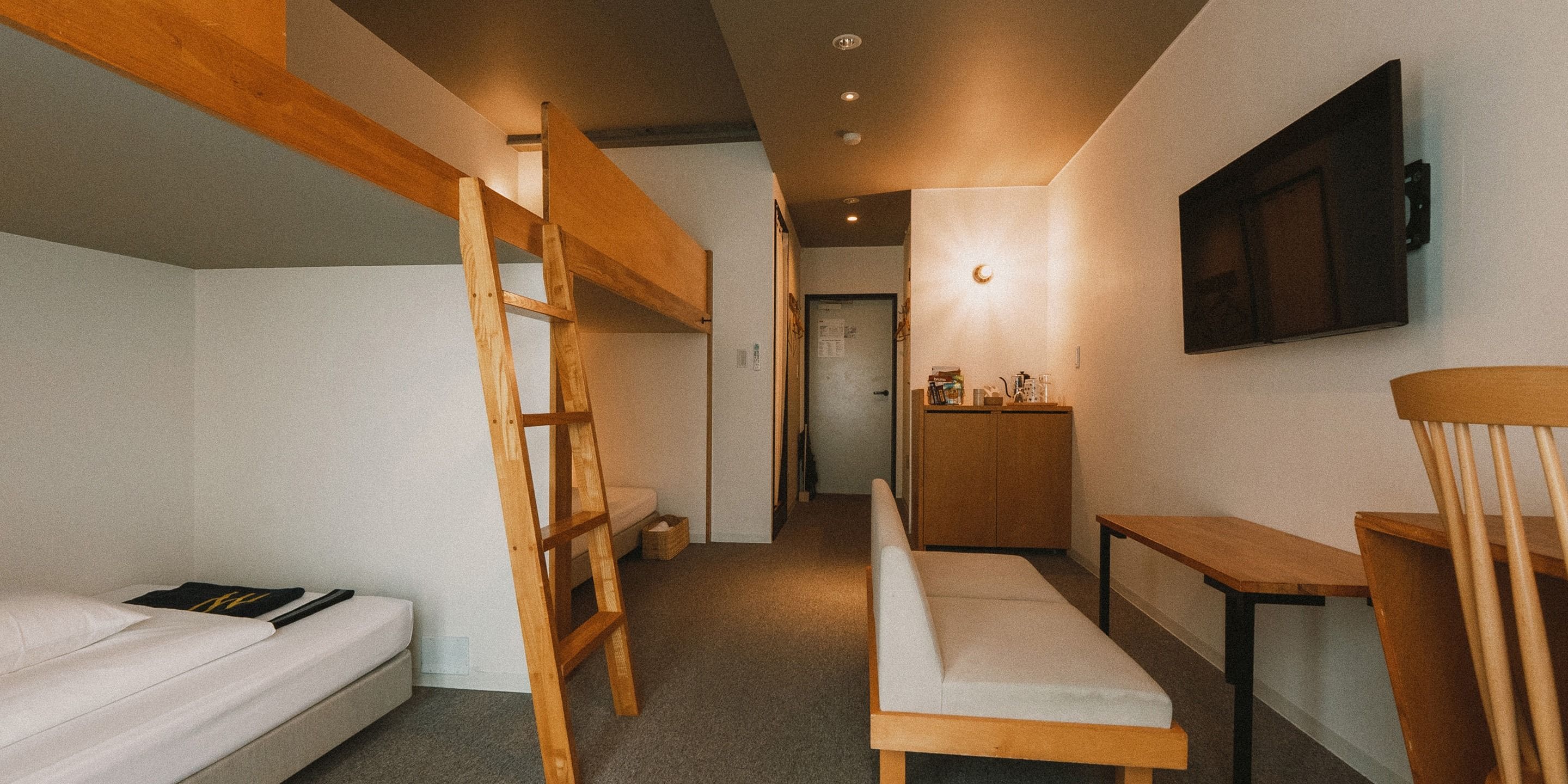 A compact room with bunk beds, a desk, a chair, and a television mounted on the wall.
