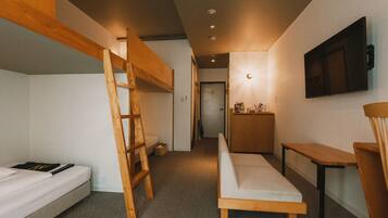 A compact room with bunk beds, a desk, a chair, and a television mounted on the wall.