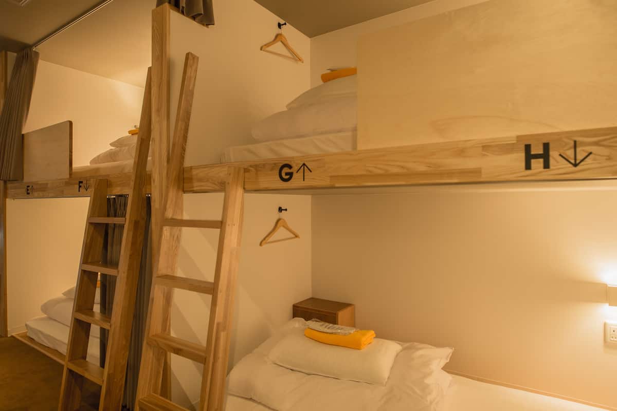 A bunk bed with a ladder, a small wooden box, and a hanging light fixture.