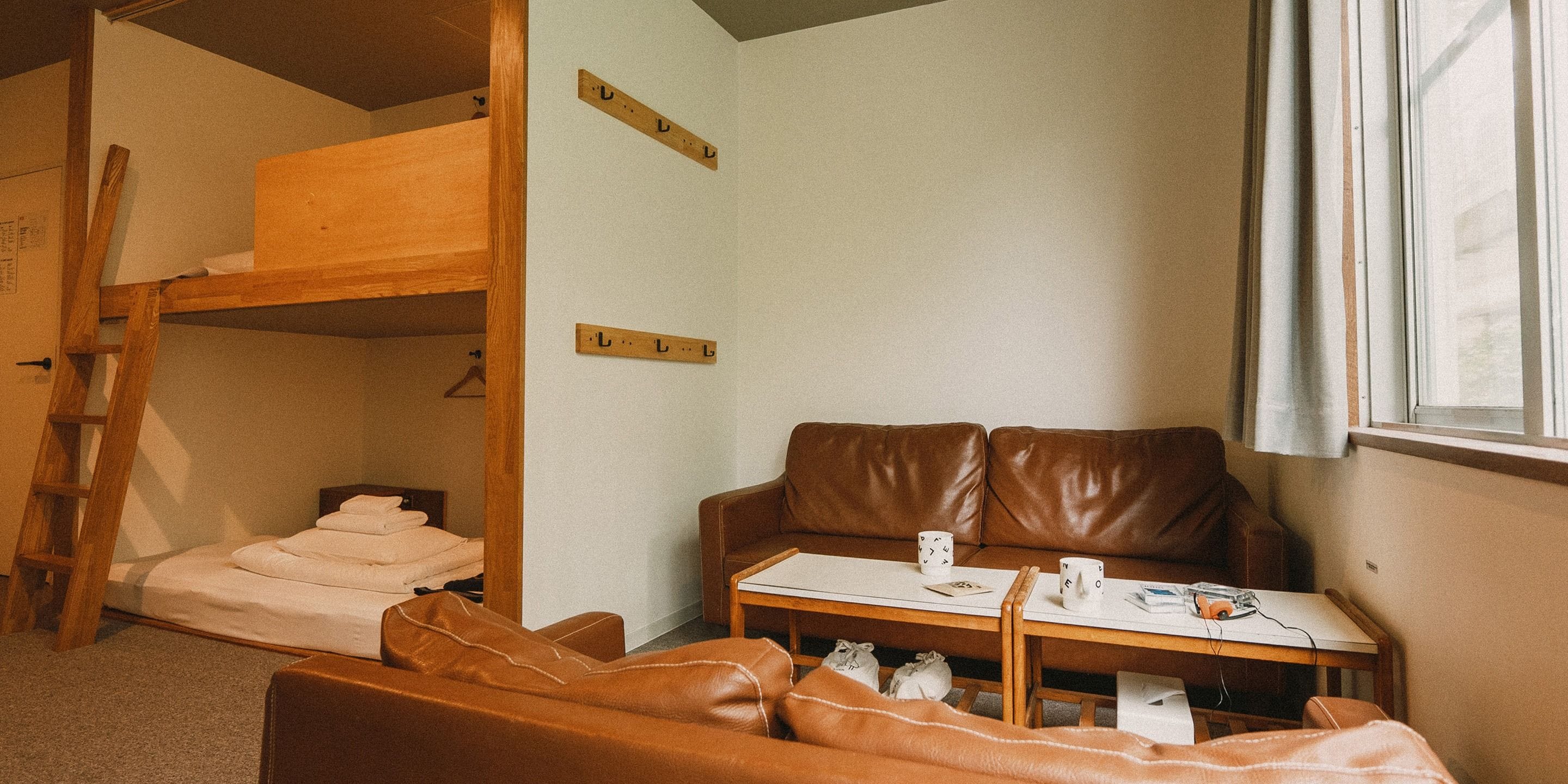 Una habitación con una cama litera, un sofá de cuero marrón, una mesita con una taza y una ventana.