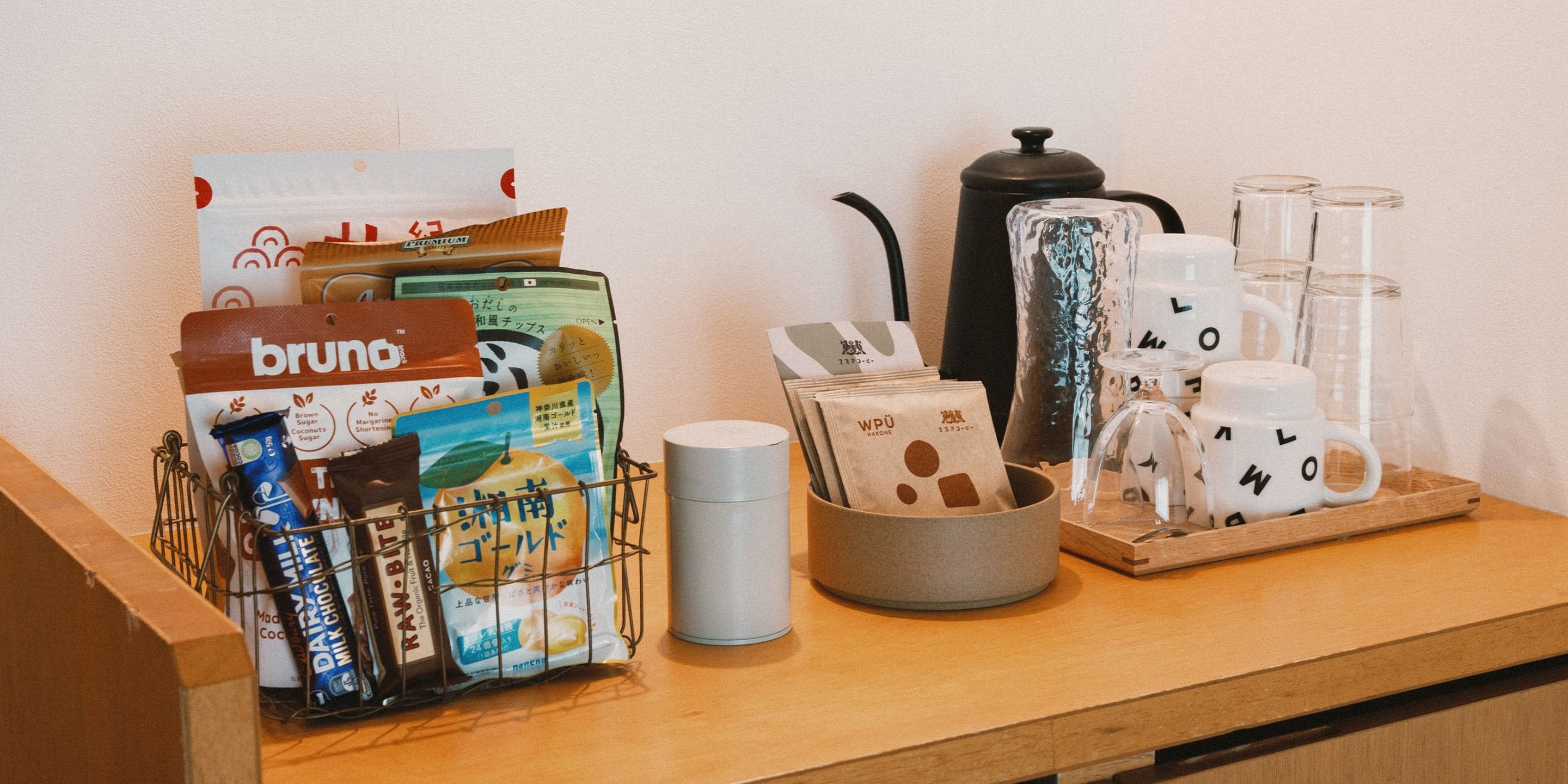 Un plan de travail de cuisine sur lequel on trouve divers objets, notamment une machine à café, une bouilloire, un moulin à café, un mousseur à lait, ainsi qu’un plateau avec des tasses à café et un pichet en verre.