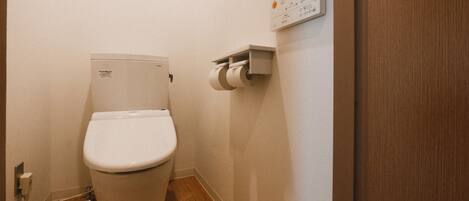 A toilet with a paper towel dispenser mounted on the wall.