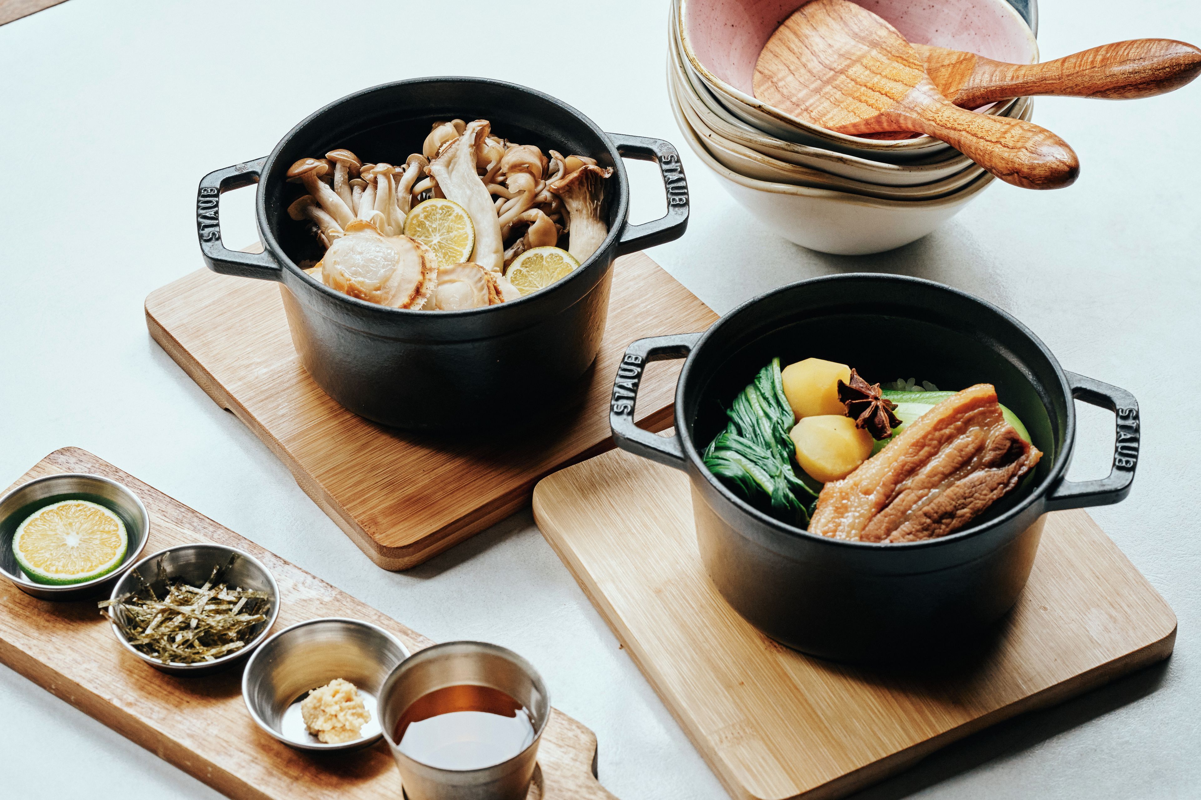 Dos ollas negras sobre tablas de madera, una con champiñones y la otra con verduras y carne.