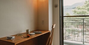 Rincón de una habitación con un escritorio de madera, una guitarra apoyada en la pared y una ventana con vista a un balcón y árboles.