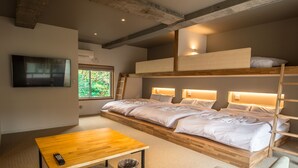 Habitación con literas, una mesa de madera, televisión y ventana con vista a la vegetación.
