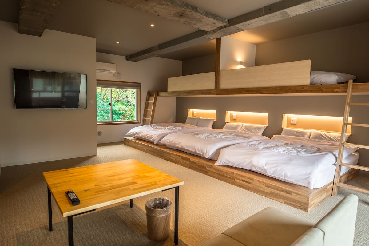 A bunk bed room with a wooden table, a TV, and a window with a view of greenery.