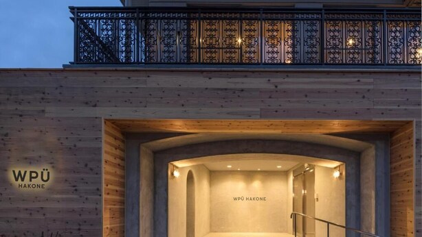 Entrada de un edificio con fachada de madera, baranda de metal y un cartel que dice 'WPÜ HAKONE'.