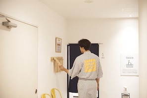A person in a patterned shirt standing in a hallway with a door, a framed picture, and a poster on the wall. - WPÜ HOTEL HAKONE (Hakone)