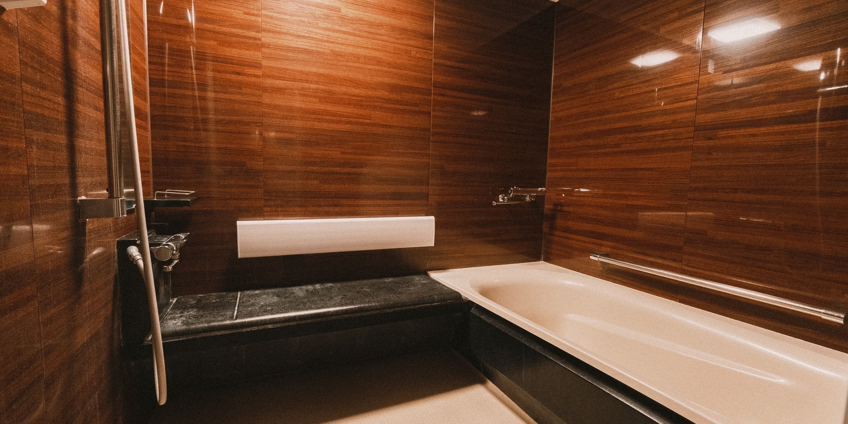 A modern bathroom with a wooden wall panel, a black bathtub, and a white towel rack.