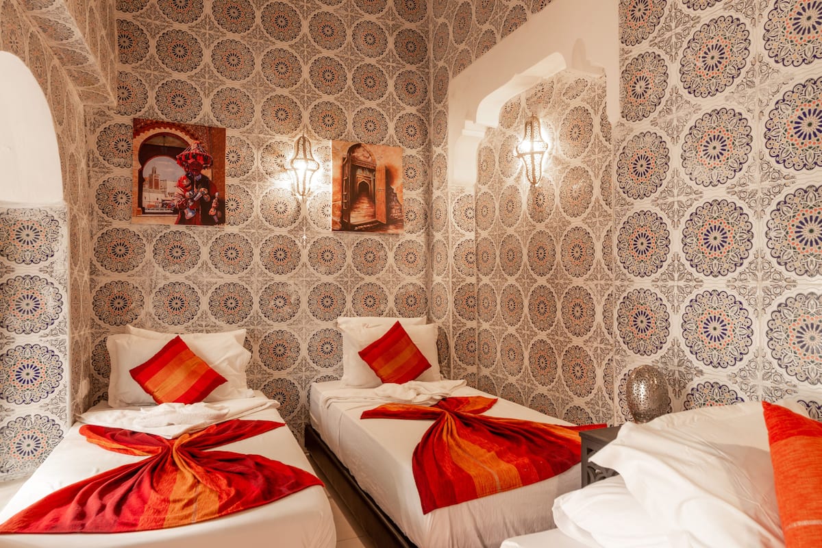 A hotel room with two beds, patterned wallpaper, and wall-mounted lights.