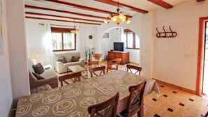 A dining area with a table set for six, wooden chairs, a chandelier, and a television in the background. - Dos Soles  - sea view holiday home with private pool in Costa Blanca (Benissa)