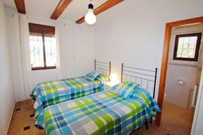 A room with two beds, a ceiling fan, and a window with curtains.