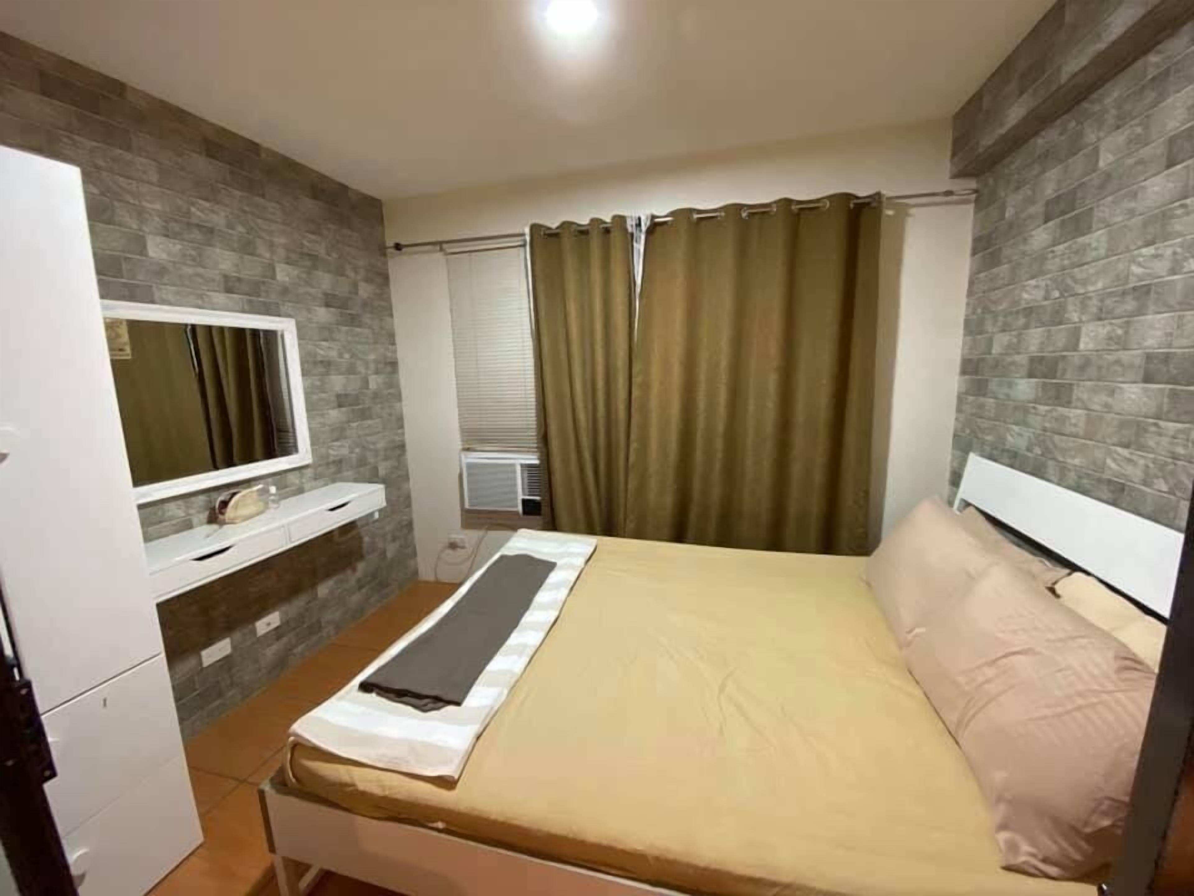 Un dormitorio con cama, televisor, ventana con cortinas y mueble de pared.