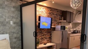 Un dormitorio con una colcha a cuadros, una toalla enrollada y un televisor que muestra una caricatura.