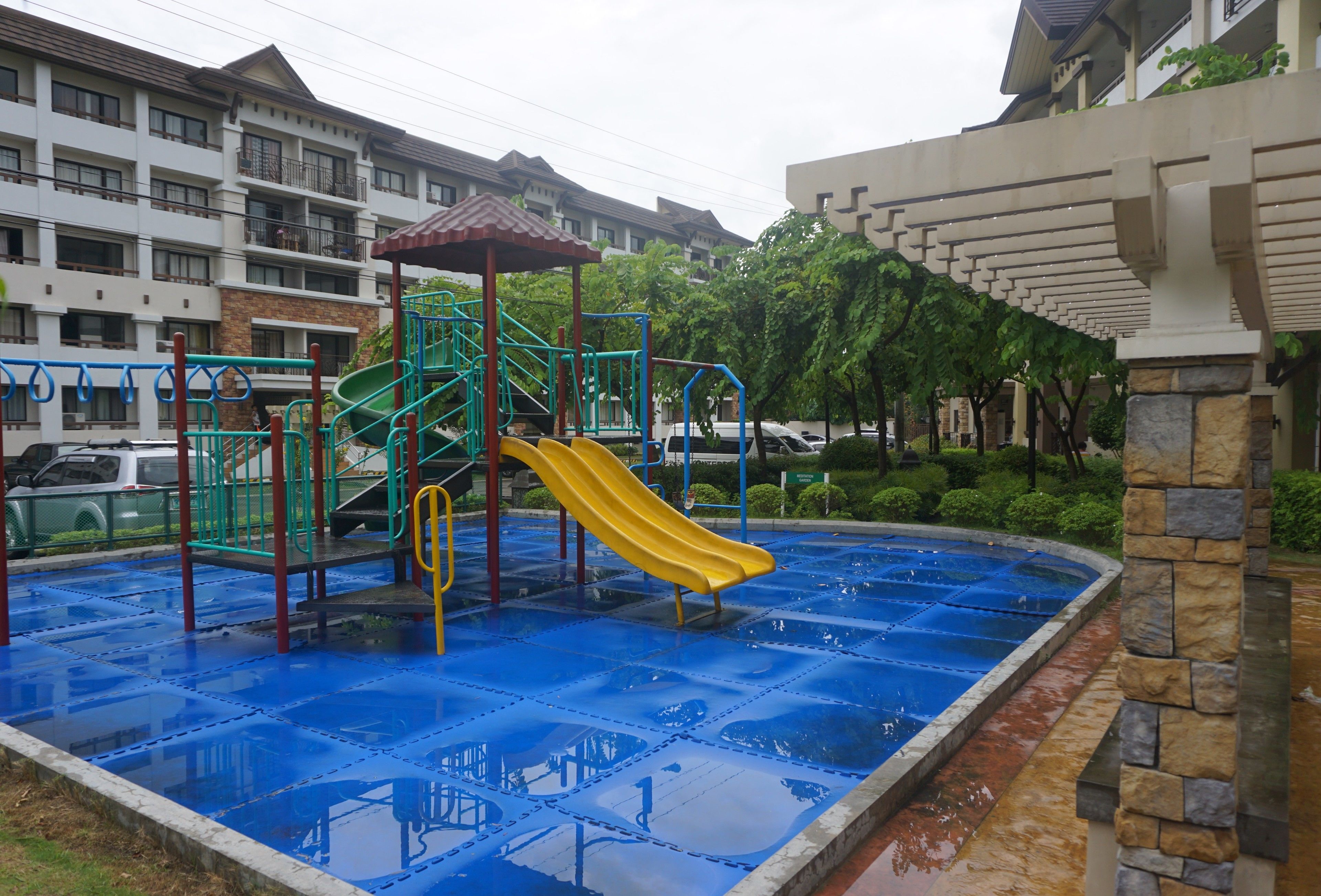 A playground with a yellow slide and climbing structures, surrounded by a pool with blue tiles.