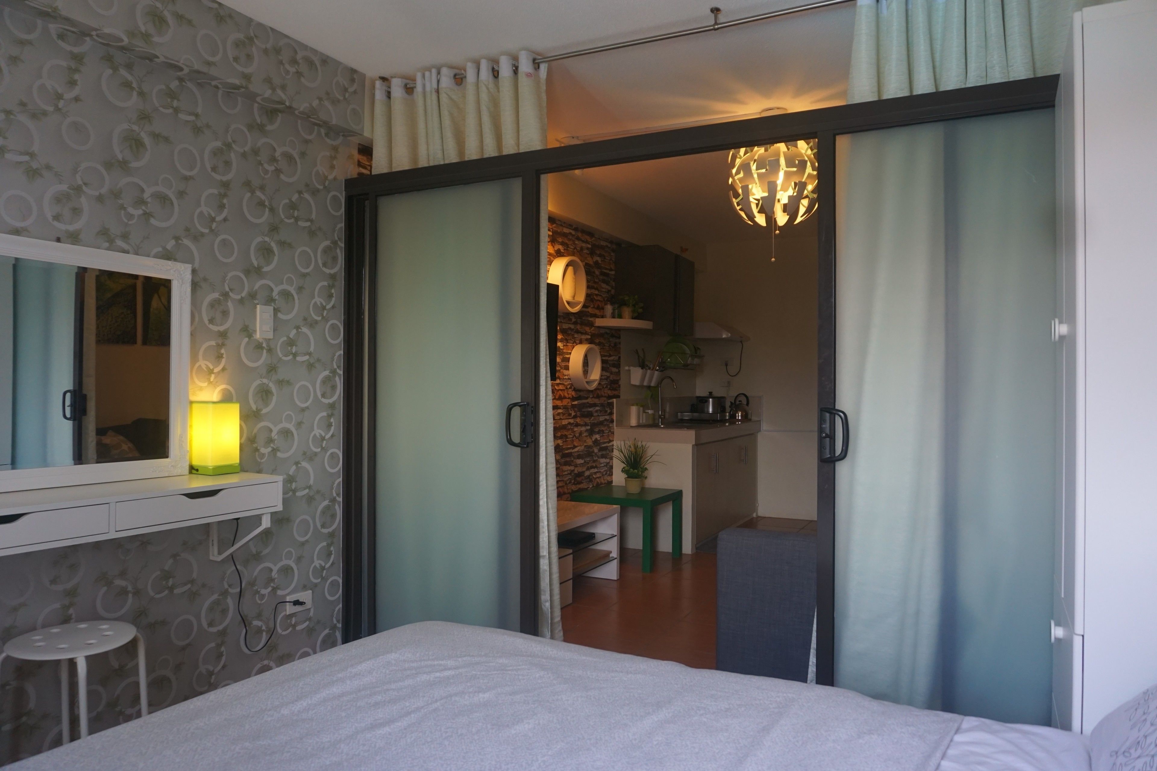 Een slaapkamer met een bed, een bureau, een stoel, een spiegel en een schuifdeur die leidt naar een keukenhoek.
