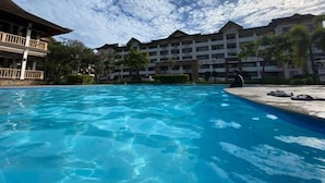Una piscina con agua azul cristalina, rodeada por un edificio con varios balcones y una gran estructura con ventanas al fondo.