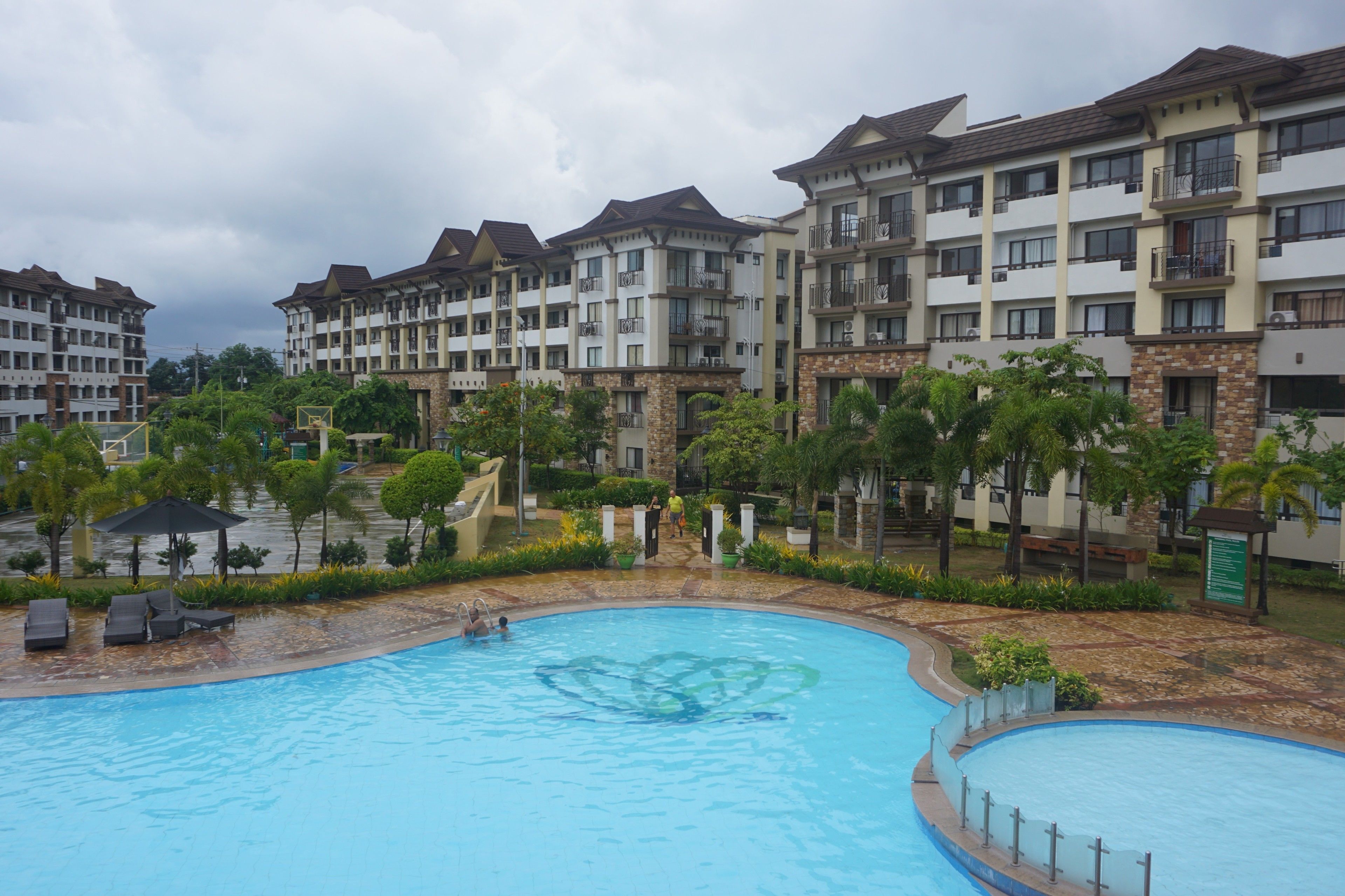 A swimming pool surrounded by a landscaped area with a multi-story building in the background.