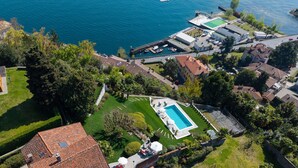 An aerial view of a coastal property with a swimming pool, a tennis court, and a marina. - Charming villa Il Motto with pool (Verbania)