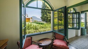 A room with a large arched window offering a view of a garden and mountains. There are two wooden chairs and a small round table. - Charming villa Il Motto with pool (Verbania)