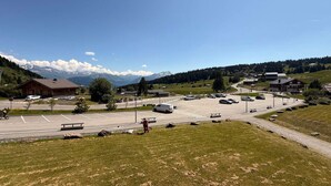 A parking lot with several cars, a building with a sign, and a mountainous landscape in the background. - Renovated cabin studio for 4, south balcony, garage included (Les Saisies)