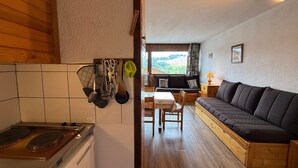 Eine kompakte Küche mit Herd, ein Esstisch mit Stühlen und ein Sofa im Wohnbereich.