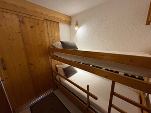 Een stapelbed met een houten hoofdbord en een kledingkast met een deurklink.