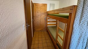 A narrow hallway with a wooden door and a bunk bed with a green mattress. - Cozy studio cabin with balcony, sleeps 5, Les Saisies (Les Saisies)
