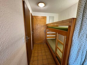 Um corredor estreito com porta de madeira e uma cama beliche com colchão verde.
