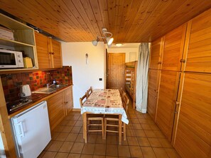 A compact kitchen with wooden cabinets, a microwave, a refrigerator, and a dining table with chairs.