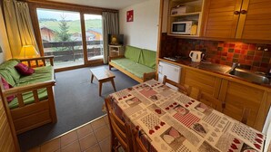 A cozy room with a green sofa, a wooden table, and a kitchen area with a microwave and sink. - Cozy studio cabin with balcony, sleeps 5, Les Saisies (Les Saisies)