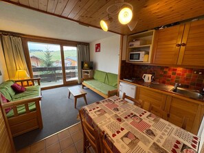 Um quarto acolhedor com um sofá verde, uma mesa de madeira e uma cozinha compacta com micro-ondas e pia.