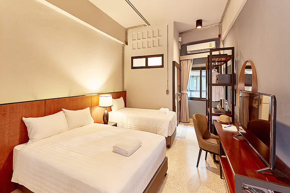 Ein Hotelzimmer mit zwei Betten, einem Schreibtisch mit Stuhl, einem Spiegel und einem Fenster.