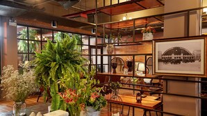 Un interior acogedor con mesas de madera, estanterías con plantas y una fotografía antigua.
