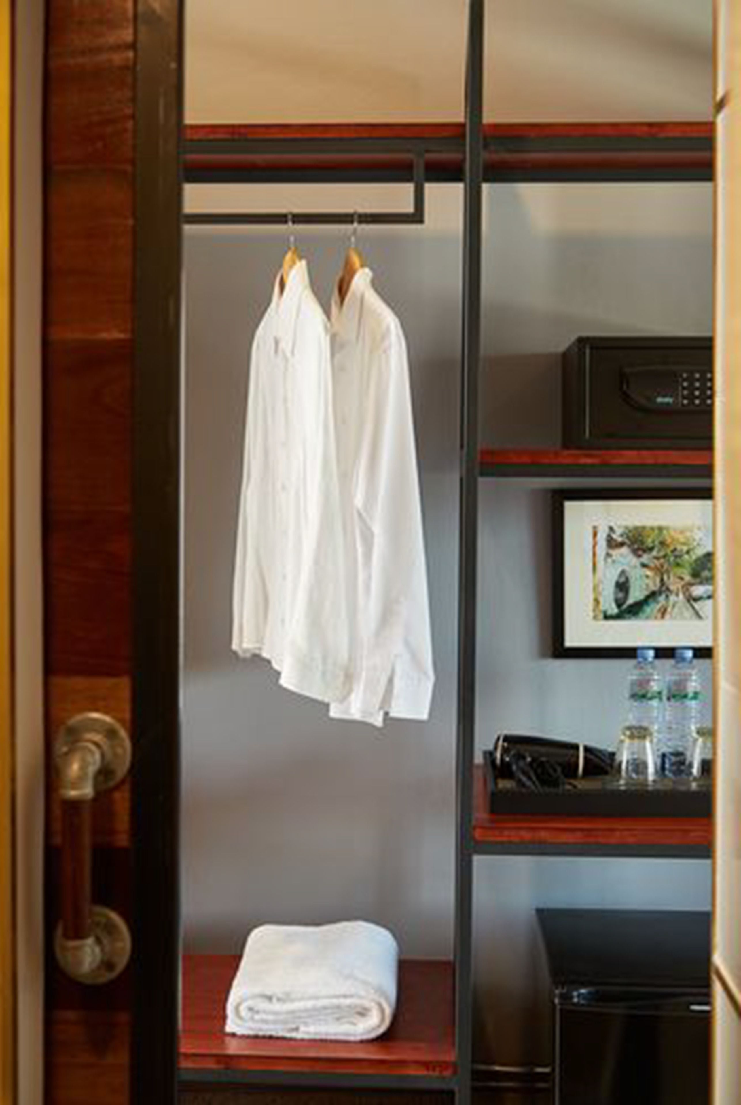 A hotel room with a wooden door, a white towel on a shelf, and a framed picture on the wall.