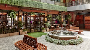Un patio interior con una fuente, bancos, plantas en macetas y una pared de ladrillo.
