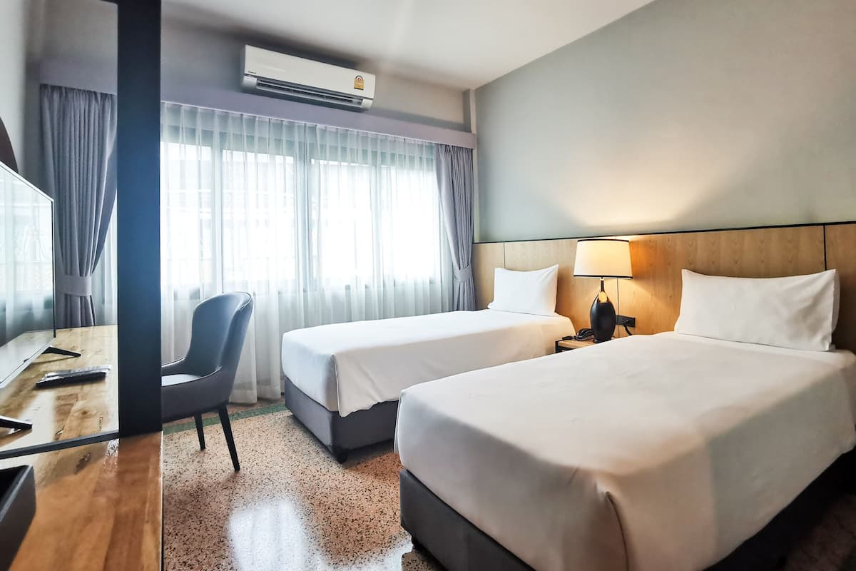 Ein Hotelzimmer mit zwei Betten, einem Schreibtisch, einem Stuhl, einer Lampe und einer Klimaanlage.