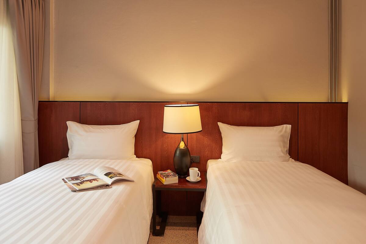 Ein Hotelzimmer mit zwei Betten, einem Nachttisch mit Lampe, einem Buch und einer Tasse.