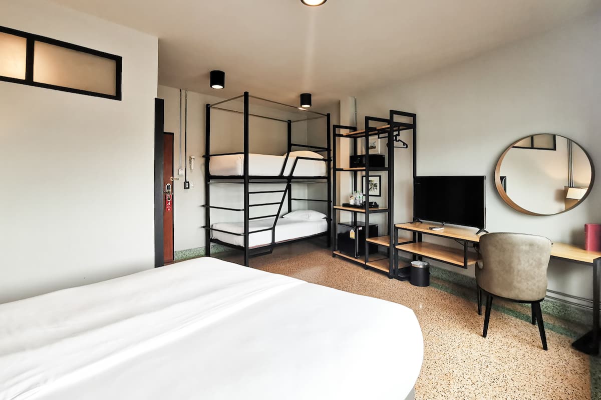Ein modernes Hotelzimmer mit Etagenbetten, einem Schreibtisch, einem Sessel, einem runden Spiegel und einem Fernseher.