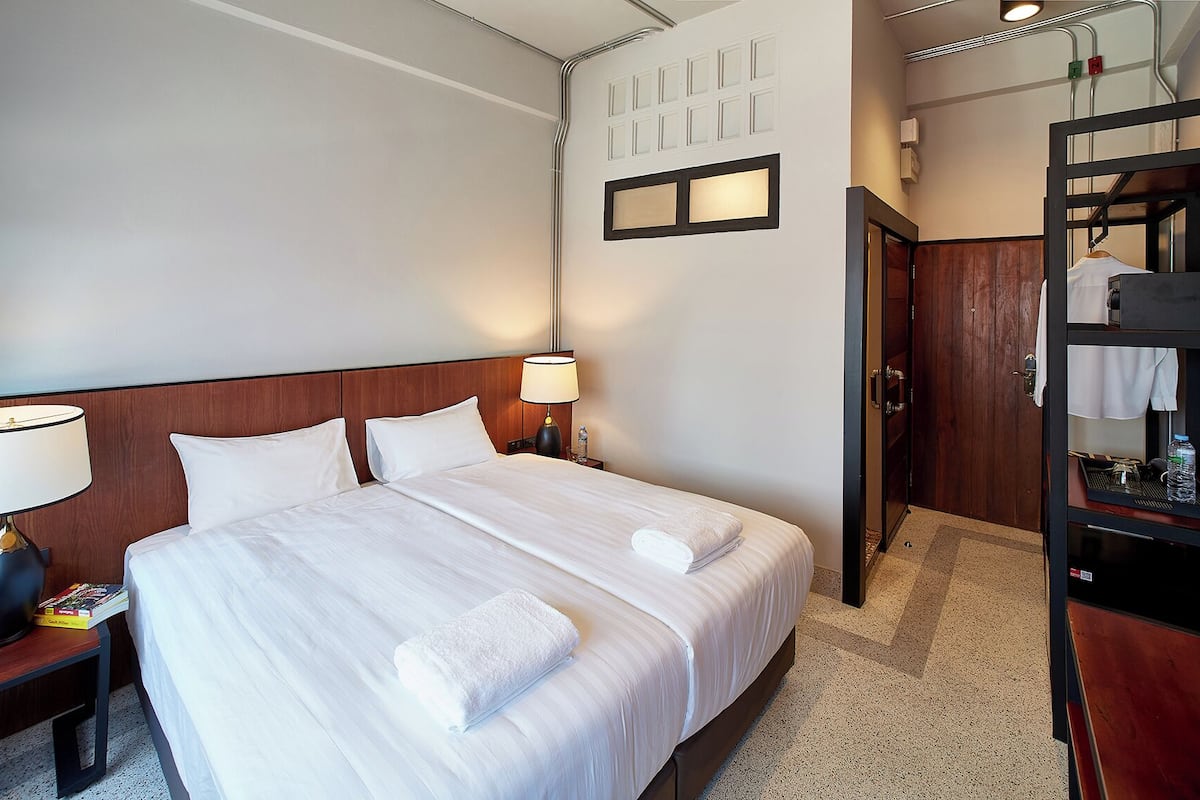 Ein Hotelzimmer mit einem großen Bett, einem Nachttisch mit Lampe, einem Holz-Kopfteil, einem Kleiderschrank und einer Tür mit Griff.