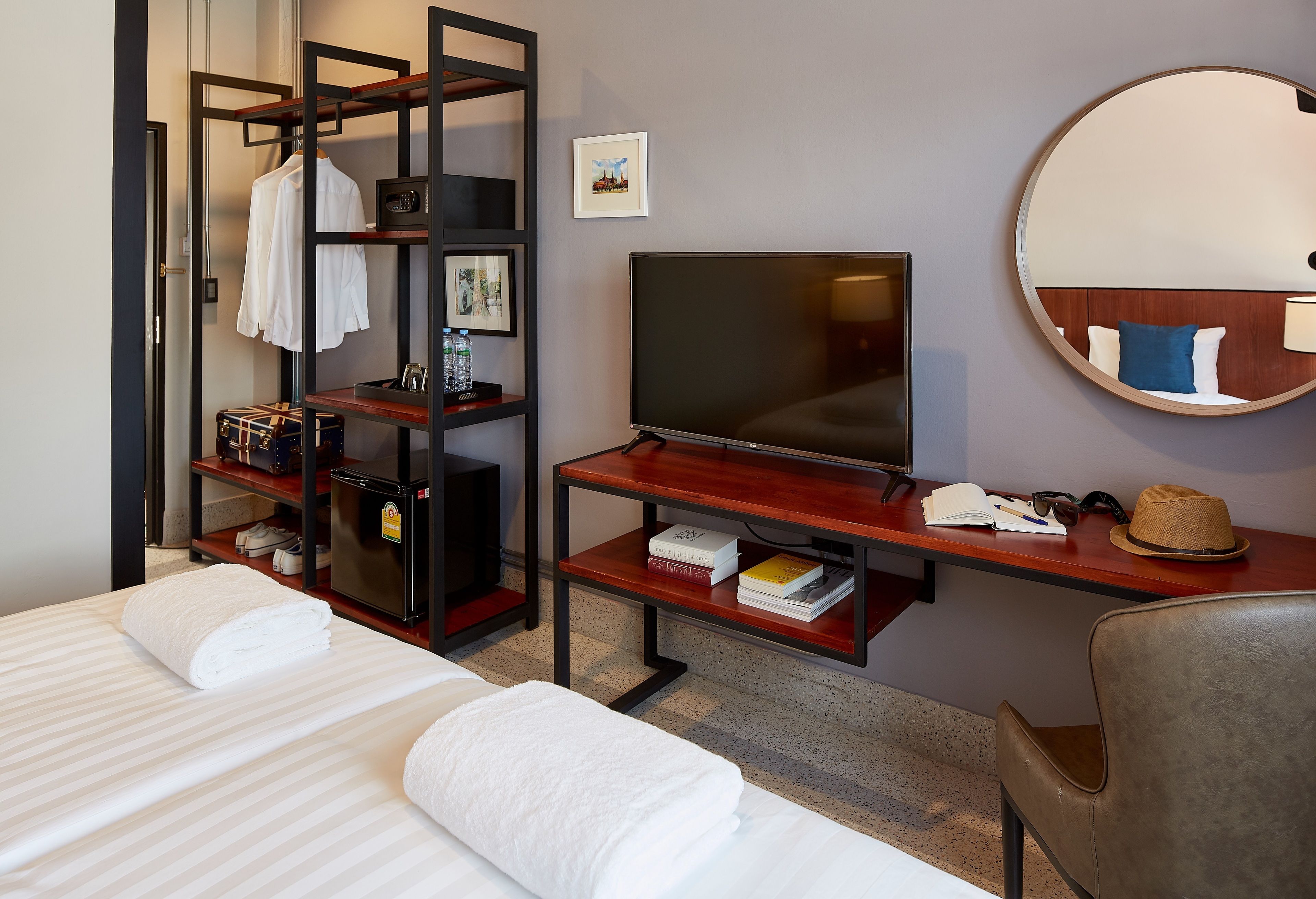 A hotel room with a bed, a desk with a TV, a mirror, and a wardrobe.