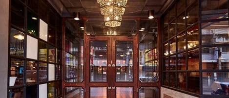 A spacious entrance with a wooden floor, a large chandelier, and glass doors leading to a bookstore.